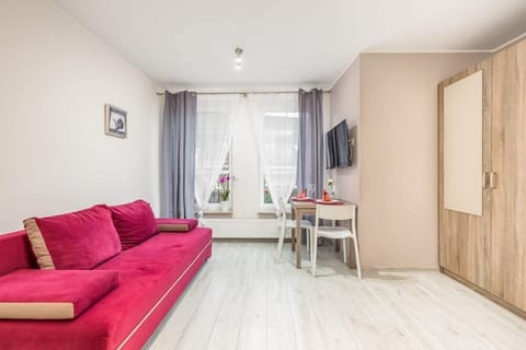 A cozy living area with a red sofa, a white table, and large windows with light curtains.

