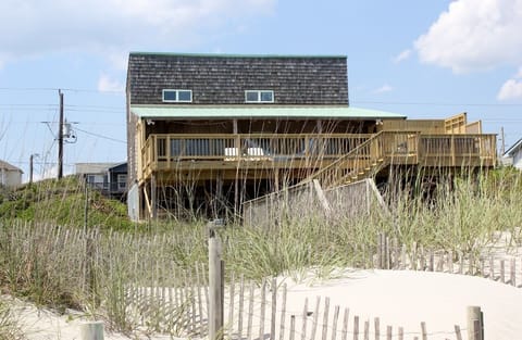 Charming oceanfront cottage with weathered shingles and expansive deck sits directly on pristine sandy dunes.