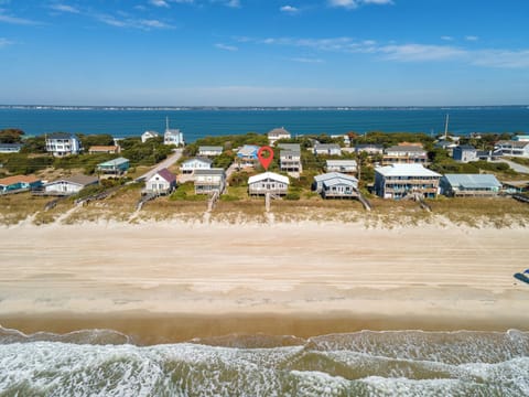 Aerial view of beachfront vacation homes nestled between pristine sandy shores and coastal waters, with the marked property positioned among charming seaside residences.