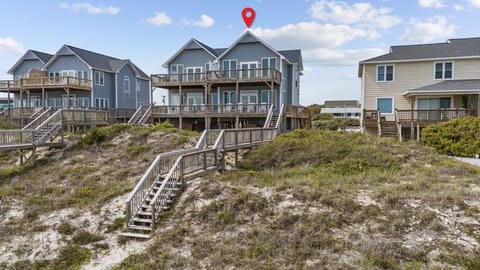 Stunning oceanfront rental home with private beach access via wooden walkway, surrounded by coastal dunes and neighboring beach houses.