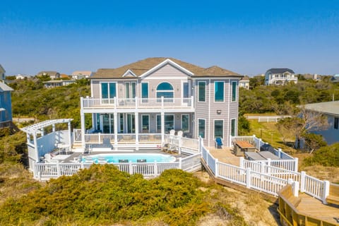 Coastal rental home with private pool, spacious decks, and multiple balconies set among natural dunes and nearby beach homes.