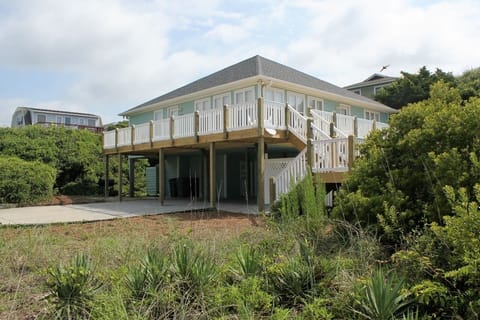 Elevated coastal home with wraparound deck and natural landscaping, situated among lush vegetation in a peaceful residential setting.