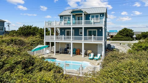 Three-story coastal home with private pool and multiple deck levels, surrounded by lush vegetation in a peaceful beachside neighborhood.