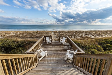 Expansive wooden deck overlooking pristine beach with white Adirondack chairs positioned for sunset viewing and ocean relaxation.