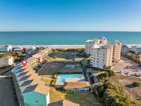 Beachfront resort complex with colorful vacation rentals, swimming pool, and direct ocean access surrounded by coastal natural areas.