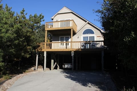 Charming elevated coastal home with wraparound balconies nestled among mature trees, offering private parking beneath the main living area.
