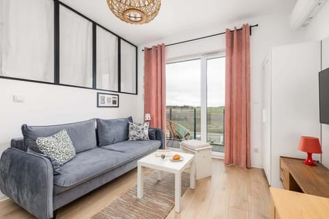 A bright living room with a gray sofa, a white coffee table, and large windows with pink curtains.

