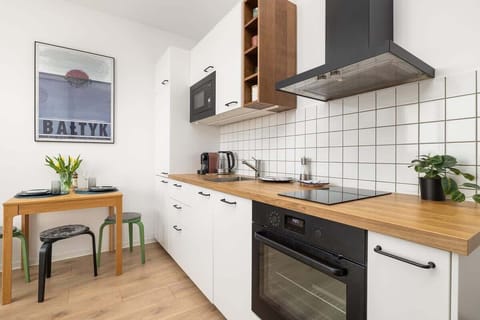 A modern kitchen with white cabinets, wooden accents, and a "Bałtyk" poster on the wall.

