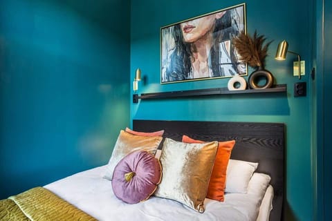 A stylish bedroom with deep teal walls, a cozy bed, and decorative pillows.

