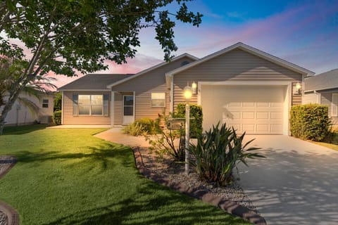 A welcoming single-story home with a spacious driveway and landscaped front yard, captured under a soft twilight sky with palm trees and tropical greenery nearby.