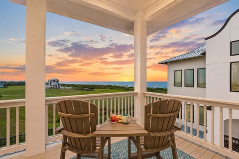 Covered balcony with Adirondack chairs and table overlooking the Gulf coastline, offering stunning sunset views and a relaxing outdoor seating area.