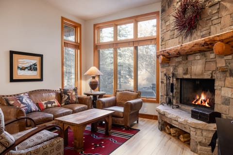 - Warm living room with rustic stone fireplace glowing  
- Leather seating and lodge style décor create cozy comfort  
- Large windows bring in natural light and forest views