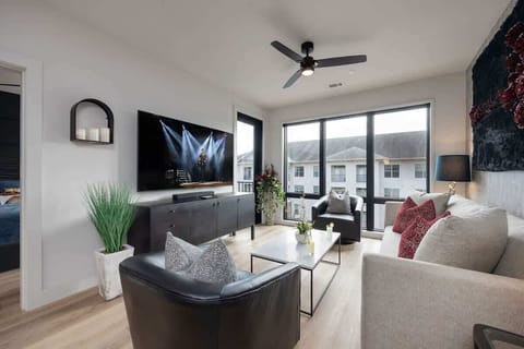 Modern open concept living area with floor to ceiling windows, designer furniture, smart TV, and access to private patio.