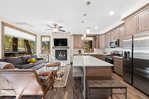 Your open-concept haven blends kitchen, living, and dining spaces with warm wood finishes, modern appliances, and a cozy fireplace for perfect relaxation.
