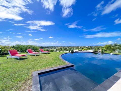 Picture of an infinity pool with red loungers set on the lawn, offering a sweeping panoramic view.
