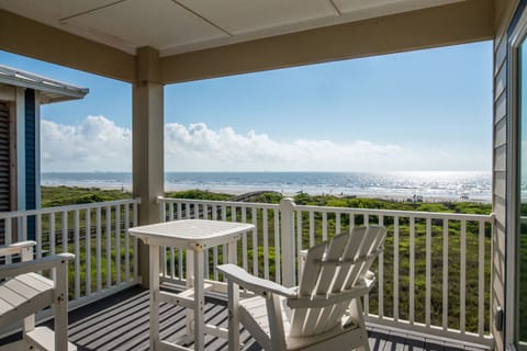 Elevated oceanfront balcony with white Adirondack seating overlooking pristine beach and endless blue horizon.