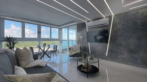The living room features a smart TV, AC, a sofa bed and also showcases the breathtaking ocean and mountain views through the ceiling to floor glass windows.