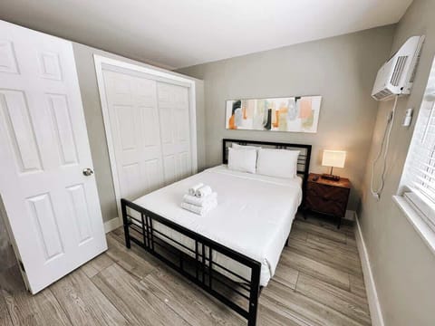 Bedroom with a comfortable bed, framed art, wall AC unit and closet storage.