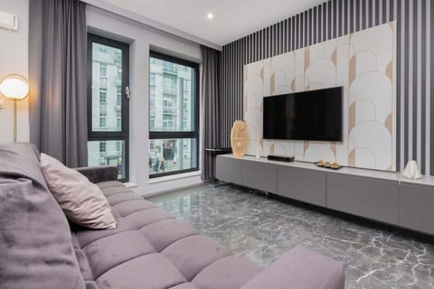 Another angle of the living space, highlighting the spacious layout, a low-profile TV console, and the tufted purple sofa.

