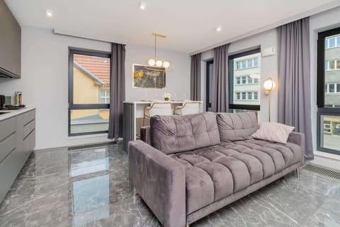 A sophisticated living area featuring a plush purple sofa, large windows, and glossy marble floors, creating a bright and stylish space.

