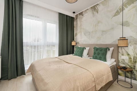 A serene bedroom with a botanical accent wall, beige bedding, and green curtains, creating a relaxing, nature-inspired ambiance.


