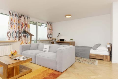 A bright living room with a grey sofa, wooden coffee table, and large windows.
