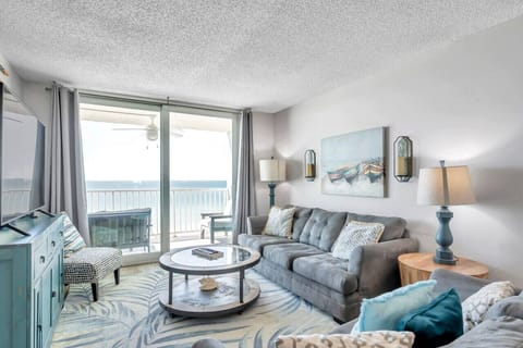 Sunlit living room w/ plush seating and sliding doors opening to the ocean-facing balcony.
