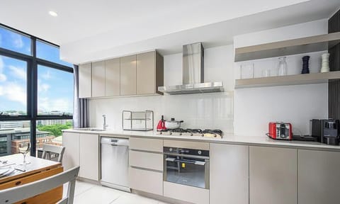 Modern kitchen with stone benchtops, cooktop, oven, rangehood, and large windows with city views.