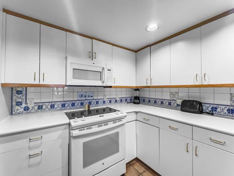 A white kitchen features white cabinets, a countertop with a toaster, a microwave above a stove, and a decorative blue and white tiled backsplash.