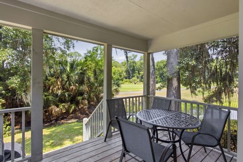 Screened porch views offer a peaceful overlook of lush palms and mossy oaks. Here, the weathered wood deck and wrought iron dining set create an ideal spot for slow coffee or evening drinks while a gentle breeze filters through the netting.