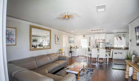 Living room,a cozy and stylish retreat with a plush neutral sofa, a patterned area rug, and a sleek coffee table. Soft wall colors and natural light create a warm ambiance,complemented by chandeliers. Personal touches include framed artwork, potted plants. It’s a perfect space for relaxation and entertaining.
