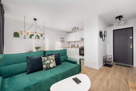 A modern living room with a green sofa, white walls, and decorative pillows.

