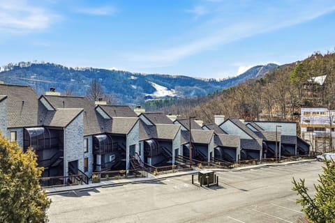 A row of modern stone townhomes nestled in a mountain valley with ski slopes visible in the distance.