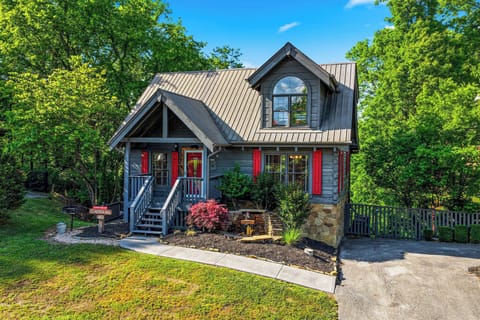 Charming mountain cabin with red shutters nestled among lush trees, featuring covered porch and landscaped grounds for a peaceful retreat.