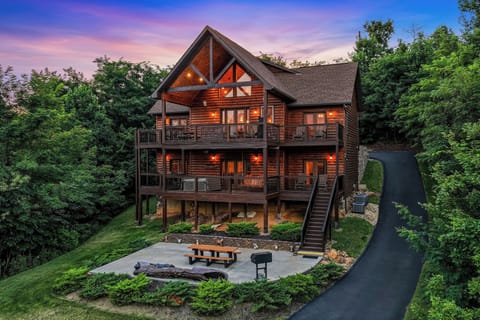 A charming log cabin retreat nestled among lush trees, featuring multi-level decks and a welcoming patio area perfect for evening gatherings as the sun sets.