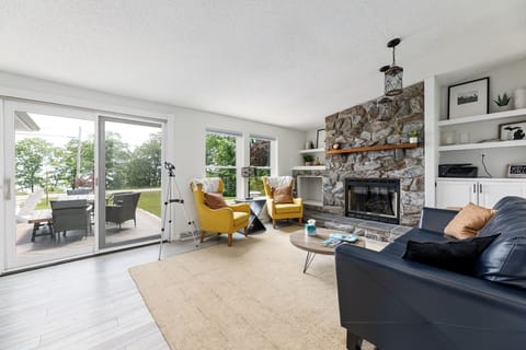 Light-filled living room w/ stone fireplace & walls of windows overlooking the bay.