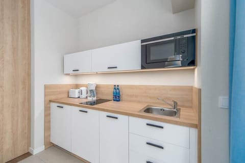A compact kitchenette featuring white cabinets, a microwave, and modern appliances, accented by warm under-cabinet lighting.

