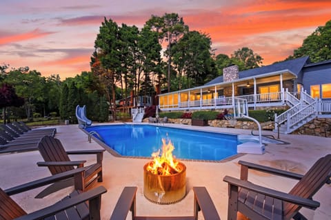 Resort-style pool at sunset with fire pit seating, loungers, and a glowing lakeside retreat feel.