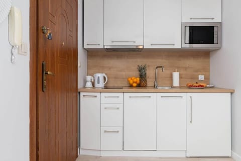 A compact kitchenette with white cabinets, a wooden countertop, and modern appliances, offering functionality.

