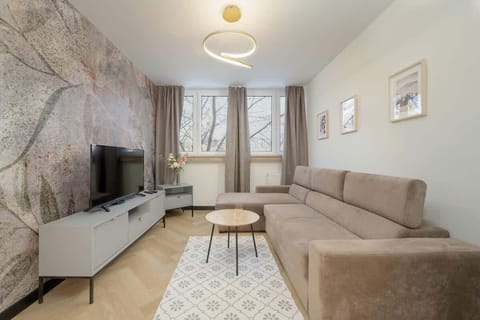 A cozy living room with a beige sectional sofa, modern coffee table, and a flat-screen TV on a sleek white console against a textured accent wall.
