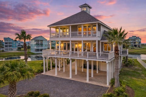 Stunning luxury beach house in Galveston with panoramic sunset views, elevated coastal design, wraparound decks, and palm-lined driveway near the ocean.