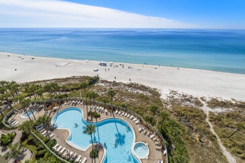 Overlooking a large pool area with direct access to a sandy beach and calm ocean waters.