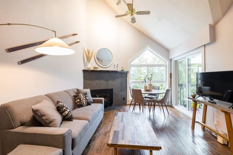 Inviting living space with natural light, a cozy fireplace nestled between the sofa and dining table. The sliding door leads to a balcony with a BBQ grill and extra seating, perfect for enjoying meals with a view. TV positioned for entertainment!