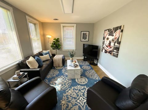 Living room with sofa seating, TV, coffee table, large windows, and wall art.