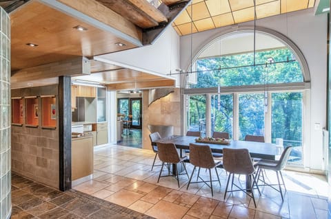 Gather around your stunning dining table beneath soaring wooden beams, where panoramic garden views frame every meal through floor-to-ceiling windows.