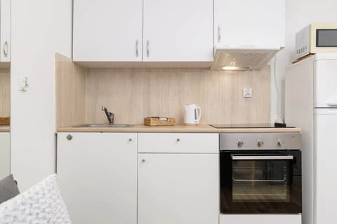 Modern kitchen with white cabinetry, electric stove, and essential appliances, creating a functional and minimalist cooking space.
