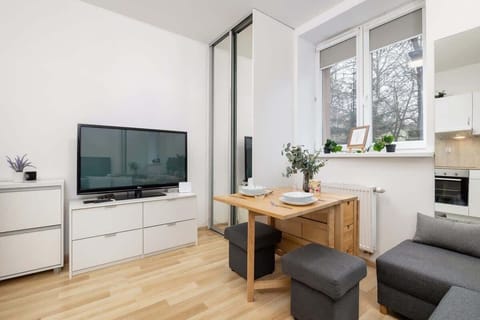Stylish living room with a flat-screen TV mounted on a white entertainment unit, complemented by potted plants near the window.
