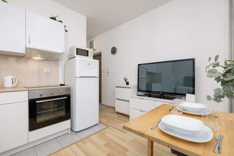 Open-plan living and kitchen area with white cabinets, a cozy gray sofa, and a wooden dining table, offering a harmonious and inviting atmosphere.
