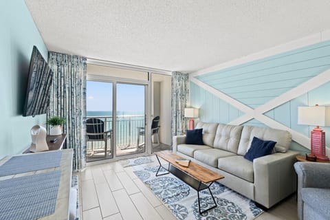Bright oceanfront living room with leather sofa, coastal décor, and large windows showcasing beautiful Myrtle Beach ocean views. Includes Smart TV and queen foam sleeper sofa, creating a clean and comfortable space to relax by the beach.