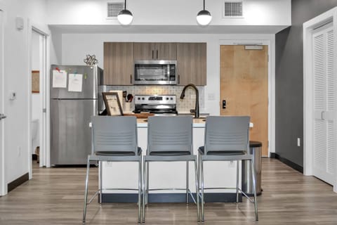 A modern kitchen space featuring with stainless appliances including a refrigerator, stove/range, dishwasher, and microwave with an oversized bar